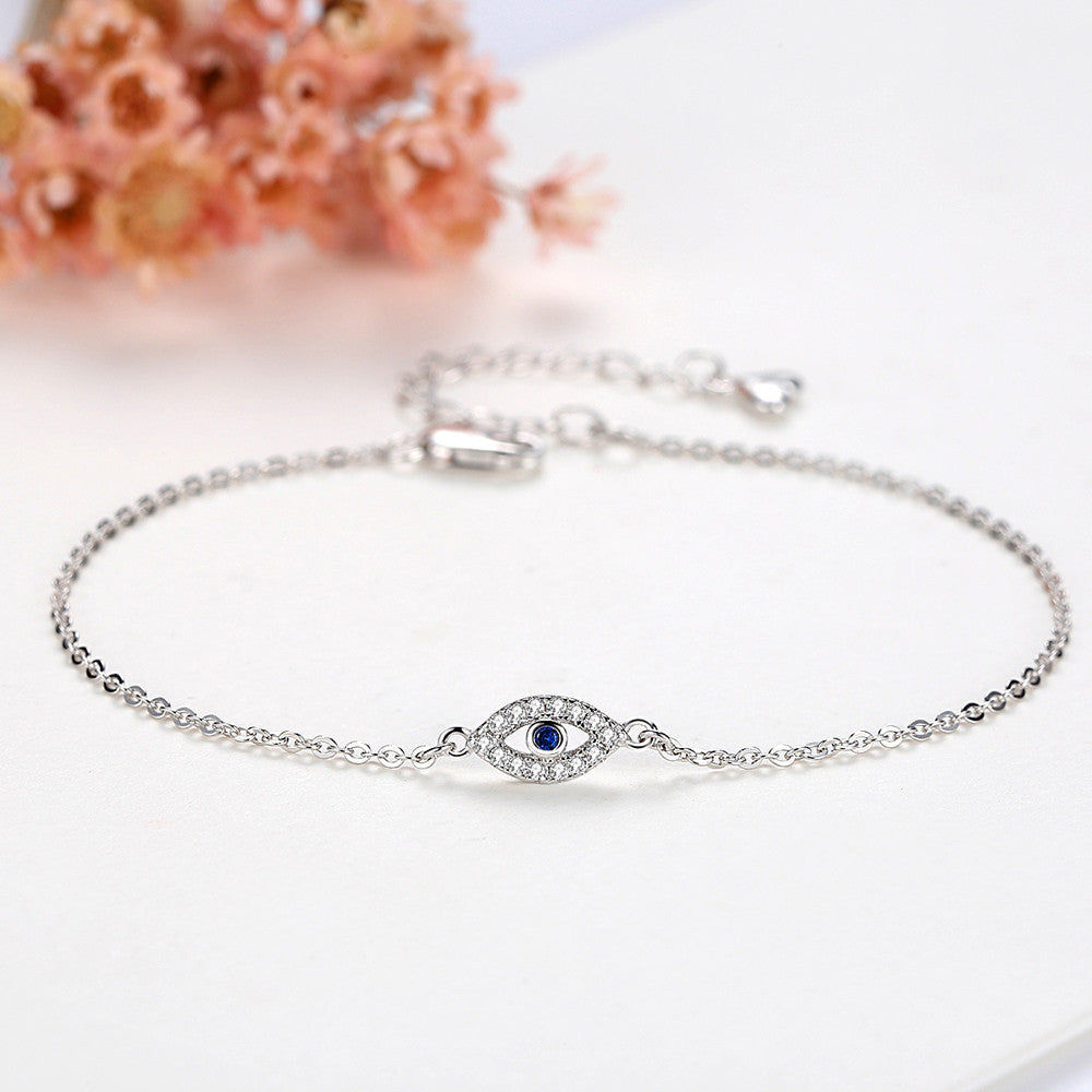 Een verfijnde close-up van de MystiekAegis armband, vervaardigd in goudkleurig metaal en voorzien van een beschermende hanger in de vorm van een oog, versierd met fonkelende kristallen en een diepblauw accent. Deze elegante en mysterieuze armband is verstelbaar en straalt stijl en betekenis uit, perfect als persoonlijk sieraad.
